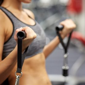 sport, fitness, lifestyle and people concept - close up of young woman flexing muscles on cable gym machine